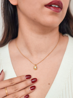Close-up of a person wearing a gold necklace with a pendant, against a neutral background.