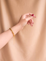 Gold bracelet on a wrist with a plain beige background