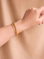 Gold bracelet on a wrist against a beige background