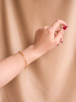 Gold bracelet on a wrist against a beige background