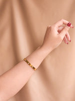 Gold bracelet on a wrist against a beige background