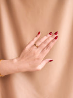 Hand with red nail polish and gold ring on a beige background