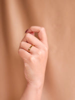 Hand wearing a gold ring on a beige background