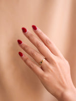 Hand with red nail polish wearing a gold ring on a beige background