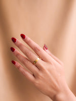 Hand with red nail polish wearing a gold ring on a beige background