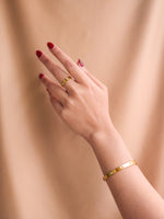 Hand wearing a gold ring and bracelet against a beige background