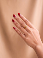 Hand with red nail polish wearing a gold ring on a beige background