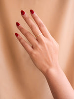 Hand with red nail polish and a gold ring on a beige background