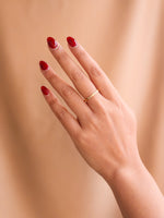 Hand with red nail polish and a gold ring on a beige background