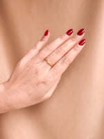 Hand with red nail polish and a gold ring on a beige background