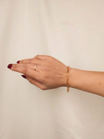 Hand wearing a gold ring and bracelet on a plain background