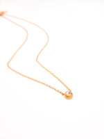 Gold necklace with a small round pendant on a white background