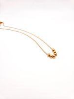 Gold necklace with three beads on a white background