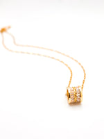 Gold necklace with a cylindrical pendant on a white background