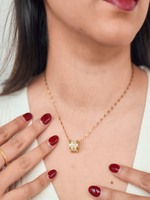 Close-up of a person wearing a gold necklace with a pendant, against a neutral background.