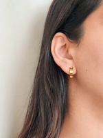Gold hoop earrings worn by a person with long dark hair against a neutral background