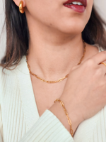 Close-up of a person wearing gold jewelry including a necklace, bracelet, and earrings.