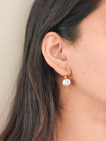 Close-up of an ear wearing a zircon and gold earring with a neutral background