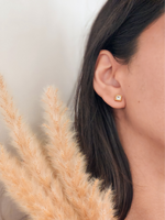 Close-up of an ear wearing a gold stud earring with pampas grass in the foreground.