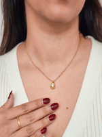 Woman wearing a gold necklace with a pendant, hand resting on chest.