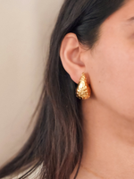 Gold earrings worn by a person with a neutral background