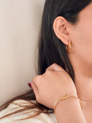 Close-up of a person wearing gold hoop earrings and a bracelet against a neutral background