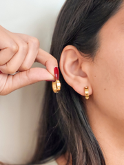 Gold hoop earrings being worn by a person with a neutral background