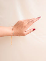 Hand wearing a gold bracelet on a beige background