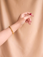 Gold bracelet on a wrist with a plain beige background