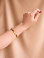 Gold bracelet on a wrist against a beige background