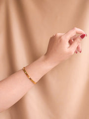 Gold bracelet on a wrist against a beige background