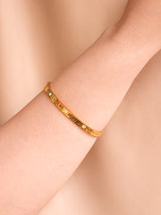 Gold bracelet with embedded stones on a person's wrist against a beige background