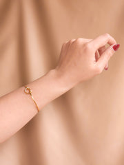 Gold bracelet on a wrist against a beige background