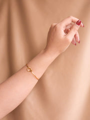 Gold bracelet on a wrist against a beige background
