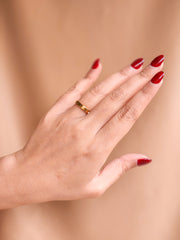 Hand with red nail polish wearing a gold ring on a beige background