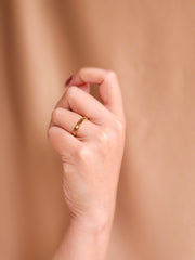 Hand wearing a gold ring on a beige background
