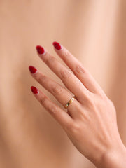 Hand with red nail polish wearing a gold ring on a beige background