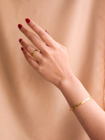 Hand wearing a gold ring and bracelet against a beige background