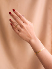 Hand wearing a gold ring and bracelet against a beige background