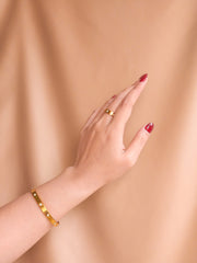Hand wearing a gold bracelet on a beige background