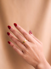 Hand with red nail polish wearing a gold ring on a beige background