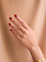 Hand with red nail polish wearing a gold ring on a beige background