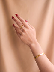 Hand wearing a gold ring and bracelet against a beige background
