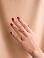 Hand with red nail polish wearing a gold ring on a beige background