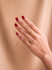 Hand with red nail polish wearing a gold ring on a beige background