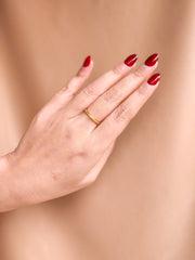 Hand with red nail polish and a gold ring on a beige background