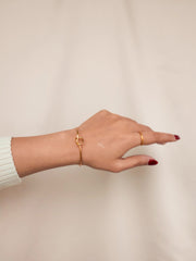 Hand wearing a gold bracelet and ring on a plain background