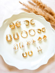 Collection of gold earrings on a white plate with dried pampas grass.