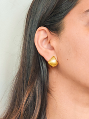 Gold shell-shaped earring worn by a person with a neutral background