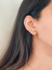 Close-up of a person wearing gold hoop earrings with a neutral background